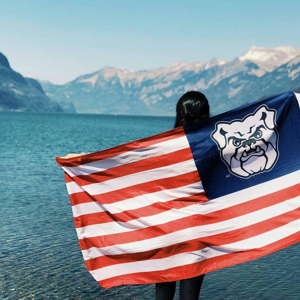 Student standing with Butler flag by lake in Switzerland