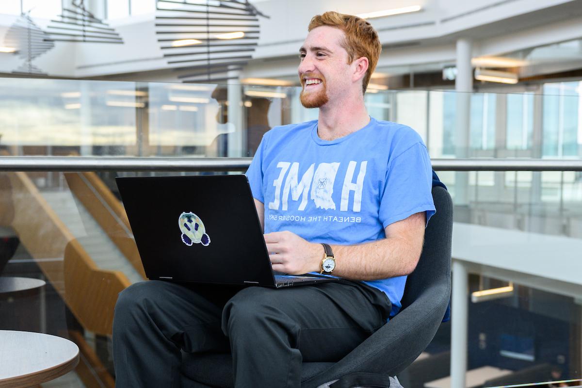 A male student works on his laptop while smiling